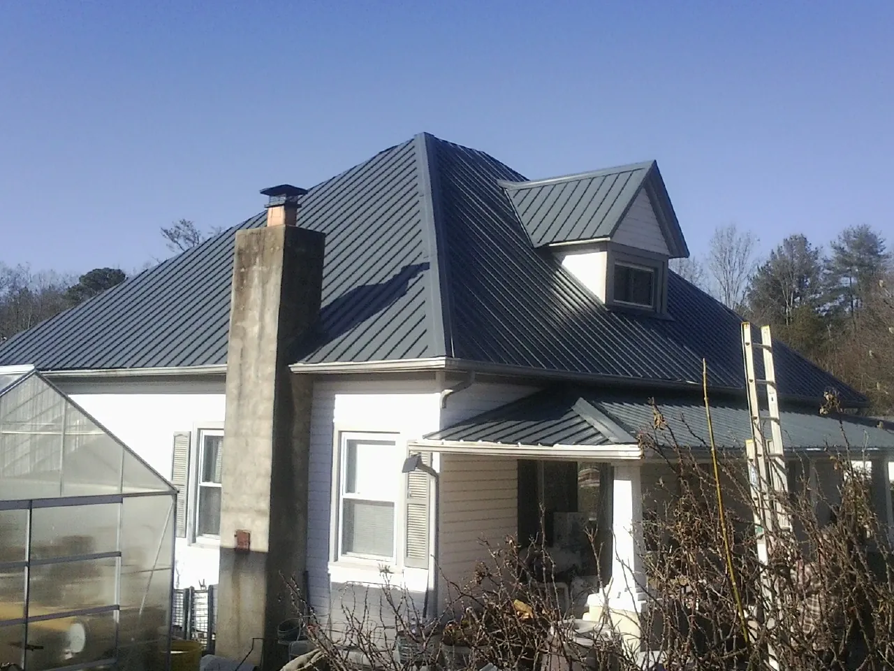 Dark blue standing seam metal roof on a white farmhouse with dormer — Slate & Tile Roof Repair by Roofing Brothers in Sarahsville