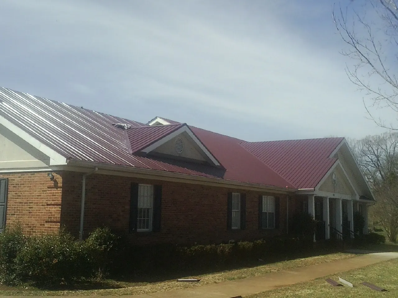 Red metal roof with gabled entries on a long brick building, from a Hail Damage Roof Repair job in Sarahsville