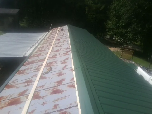 Old rusted panels beside newly installed green metal roofing — Wind Damage Roof Repair by Roofing Brothers in Sarahsville