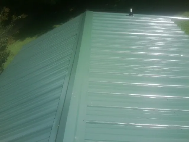 New green metal panels meeting at the ridge of a roof — Flat Roof Repair work by our crew in Sarahsville