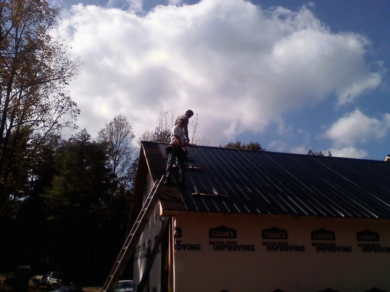 Roofer fastening dark metal panels high against a cloudy sky, from a Roof Inspection job in Sarahsville