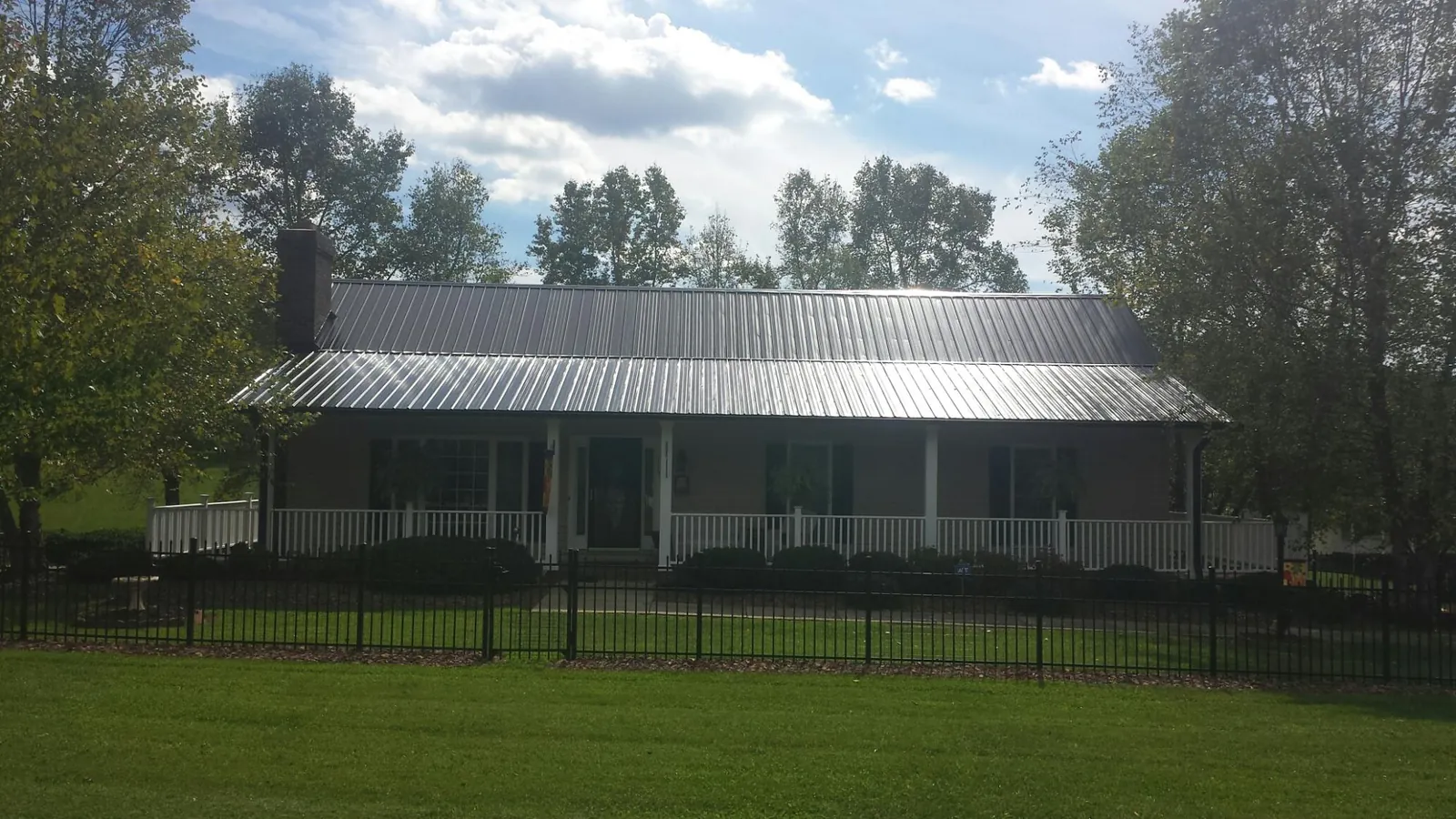 Gray metal roof on a brick ranch with a full width front porch — Gutter Guard Installation work by our crew in Sarahsville