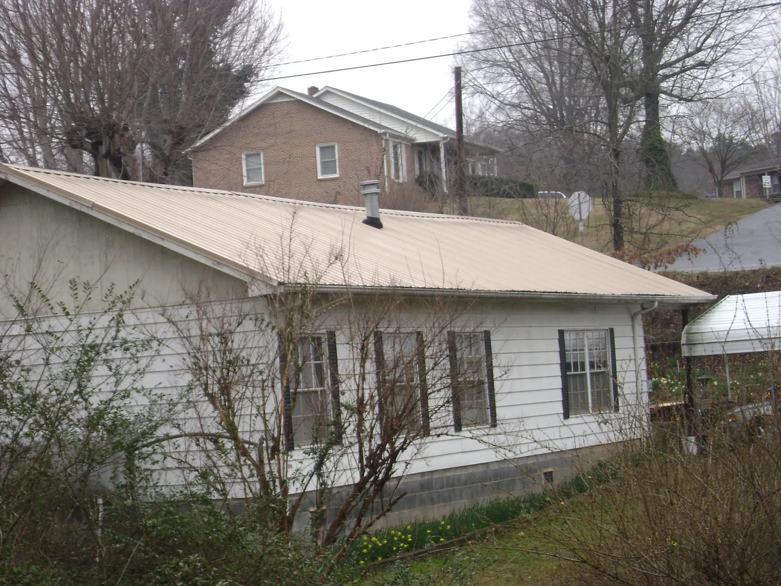 Tan metal roof on a white sided house set into a hillside — Commercial Roofing by Roofing Brothers in Sarahsville