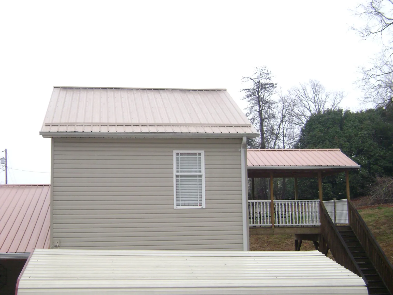 Tan metal roofs on a two story addition and attached porch, from a Roof Replacement job in Sarahsville
